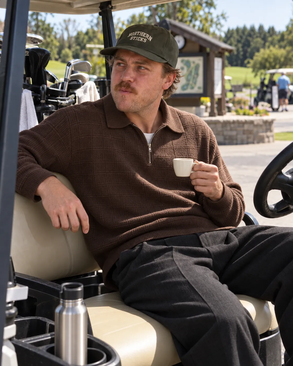 A guy in a Northern Sticks cap with an espresso, sitting in a golf cart