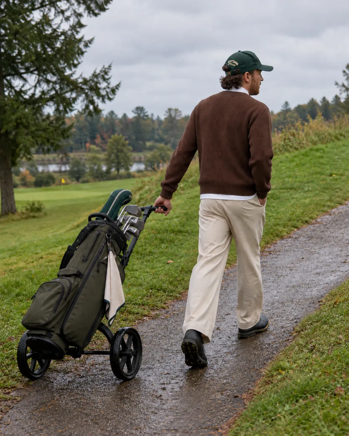 A golfer walking a cart path, pulling his clubs on a push cart