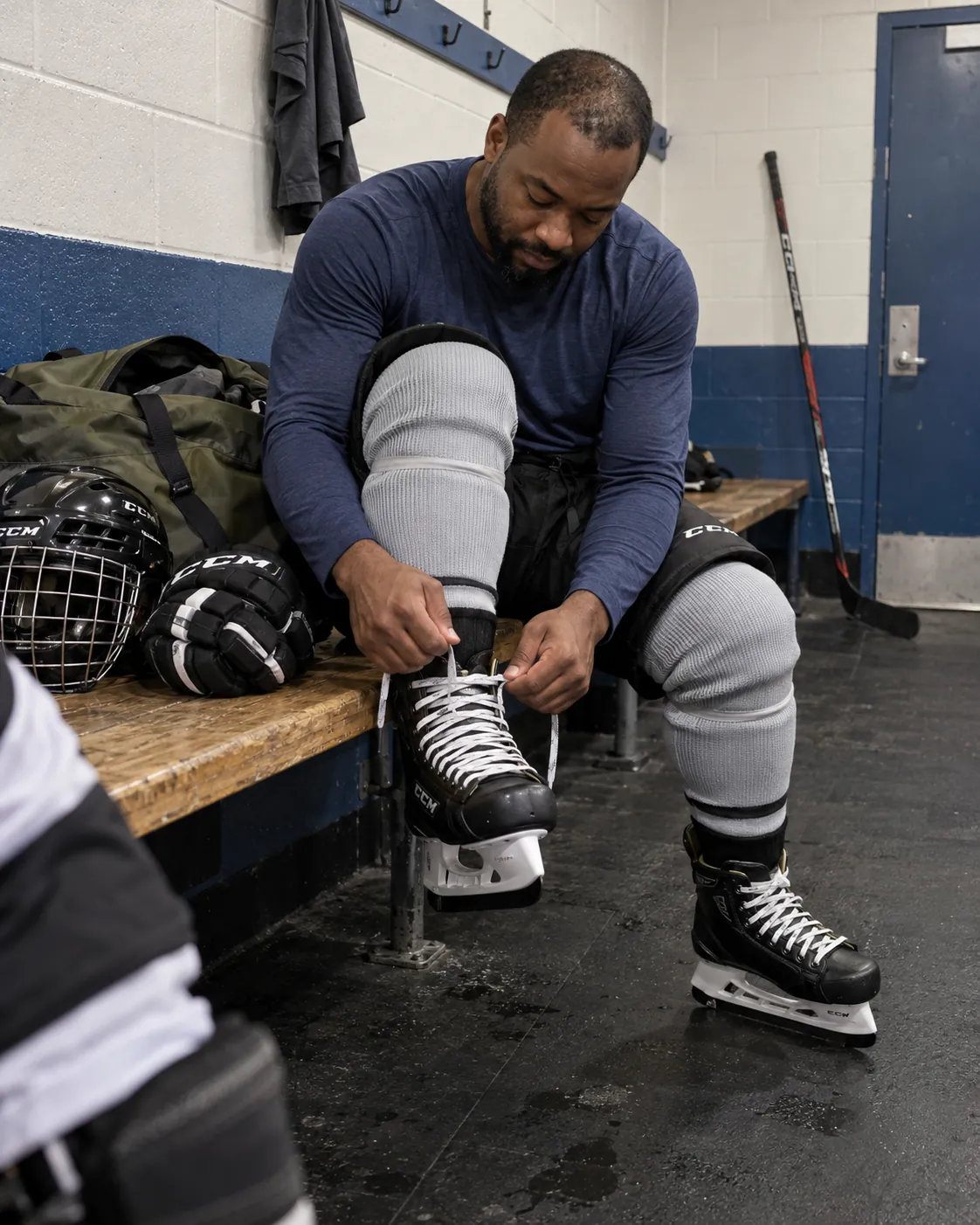Lacing up skates in a dressing room, a gear bag on the bench